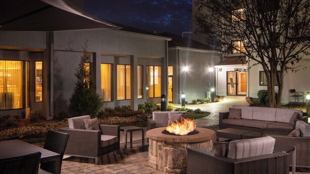 An outdoor patio area with wicker furniture, a stone fire pit, and a view of the building's entrance.