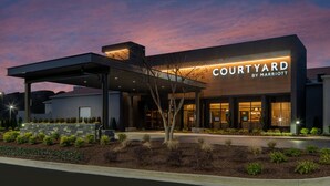 A modern Courtyard by Marriott hotel with a covered entrance, landscaped garden, and a clear sky at dusk.