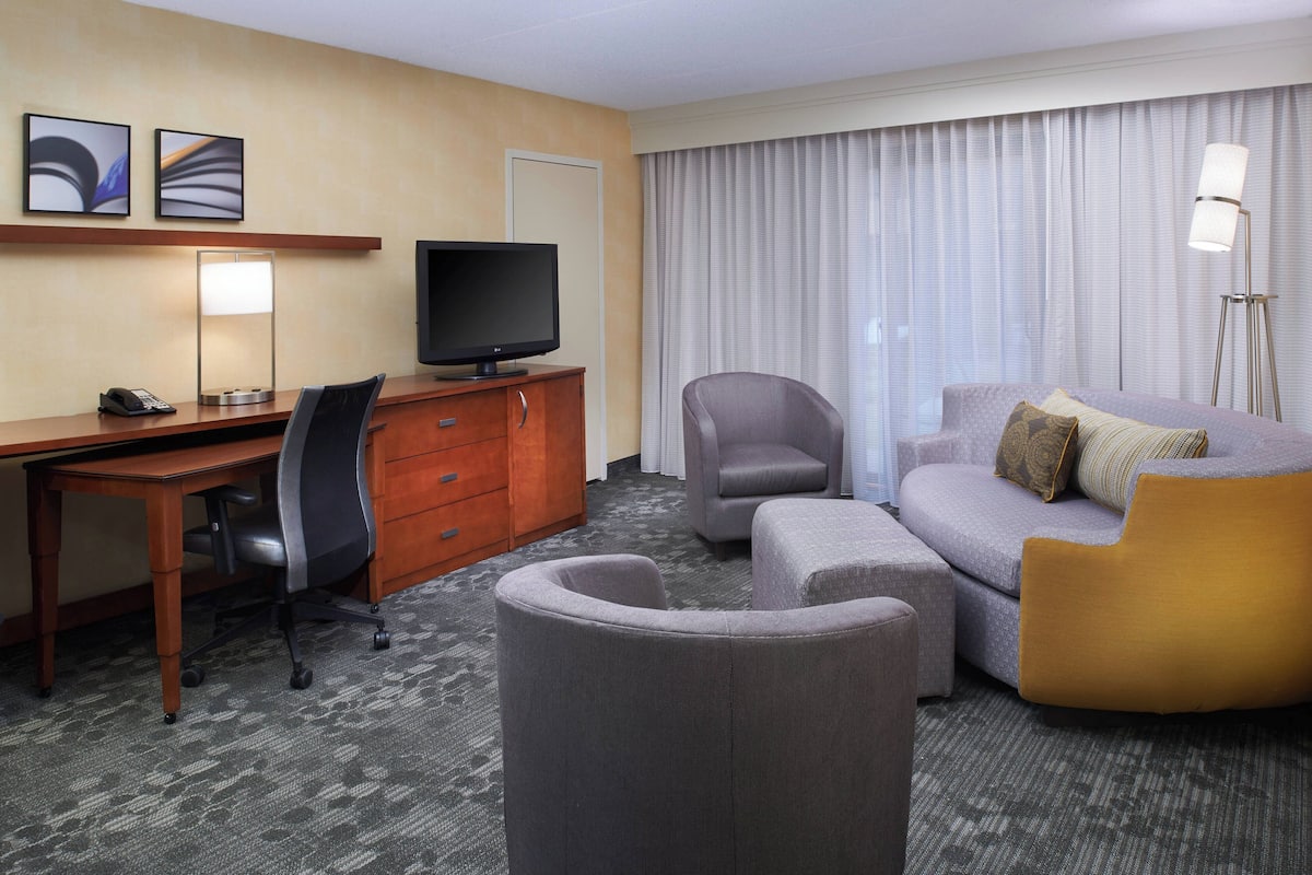 A hotel room with a desk, television, and seating area.