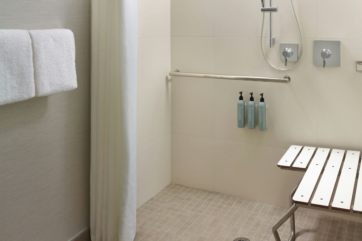 A bathroom with a shower, a towel rack with towels, a hand dryer, and a small table with a tray.
