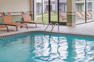 An indoor swimming pool with lounge chairs and a view of the outside.