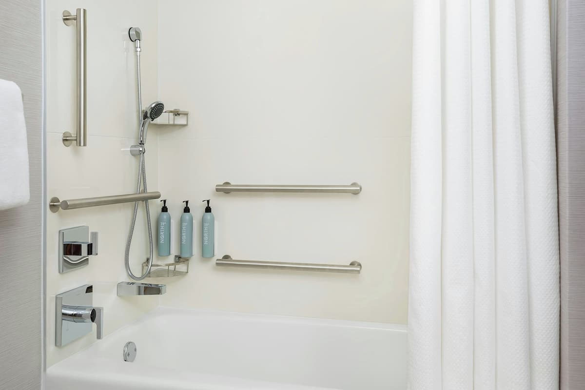 A bathroom with a bathtub, grab bars, a showerhead, and toiletries.
