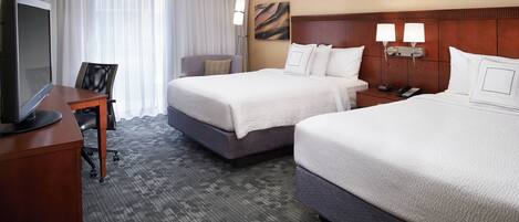 A hotel room with two beds, a desk with a television, a chair, and a nightstand with a phone and lamp.