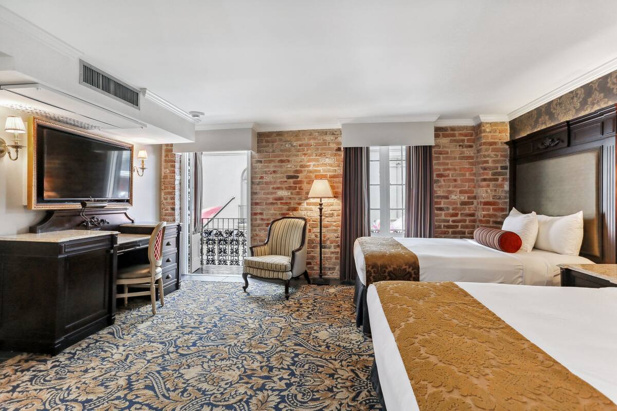 A hotel room with a large bed, a desk with a TV, a chair, and a patterned carpet.