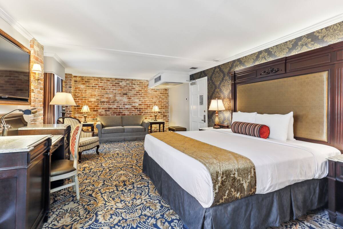 A hotel room with a large bed, a sofa, a desk, and a brick wall.