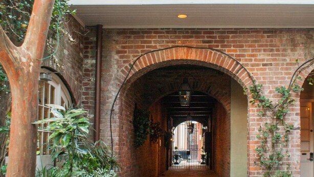 A brick building with arched doorways and a balcony with white railings. - Place d'Armes Hotel (New Orleans)