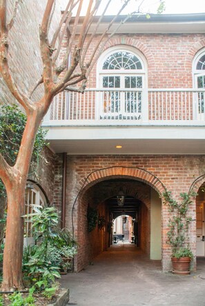 A brick building with arched doorways and a balcony with white railings. - Place d'Armes Hotel (New Orleans)