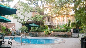 A pool area with a brick wall, outdoor seating, and a building with a balcony in the background. - Place d'Armes Hotel (New Orleans)