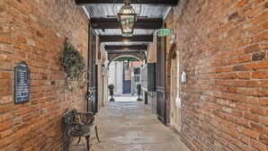 A brick corridor with an exit sign, a bench, and a lantern. - Place d'Armes Hotel (New Orleans)