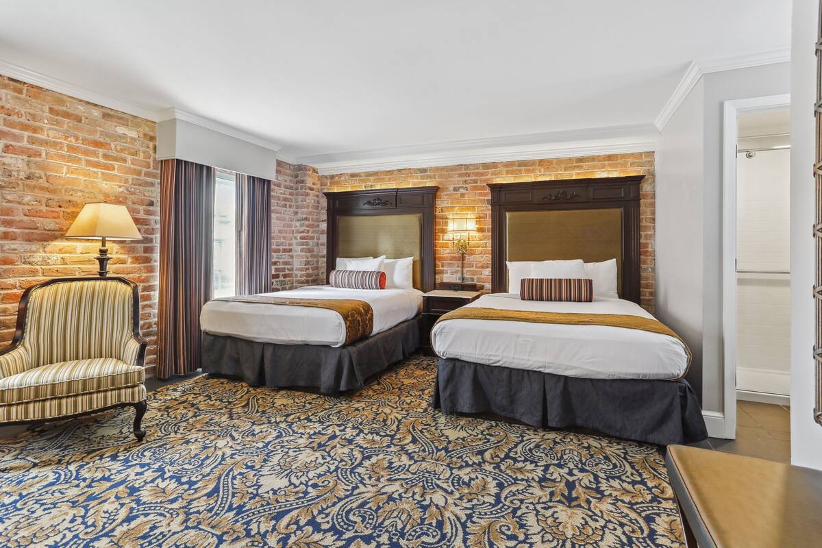A hotel room with two beds, a chair, a lamp, and a patterned carpet.