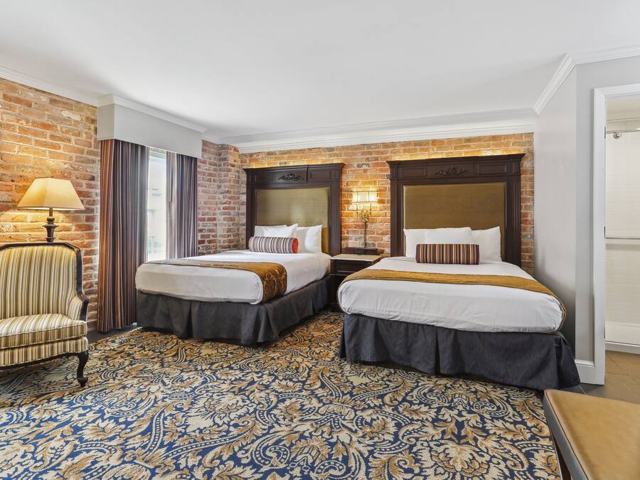 A hotel room with two beds, a chair, a lamp, and a patterned carpet.