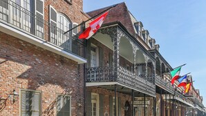 A historic hotel with a brick facade, a balcony with ornate metal railings, and multiple flags displayed. - Place d'Armes Hotel (New Orleans)