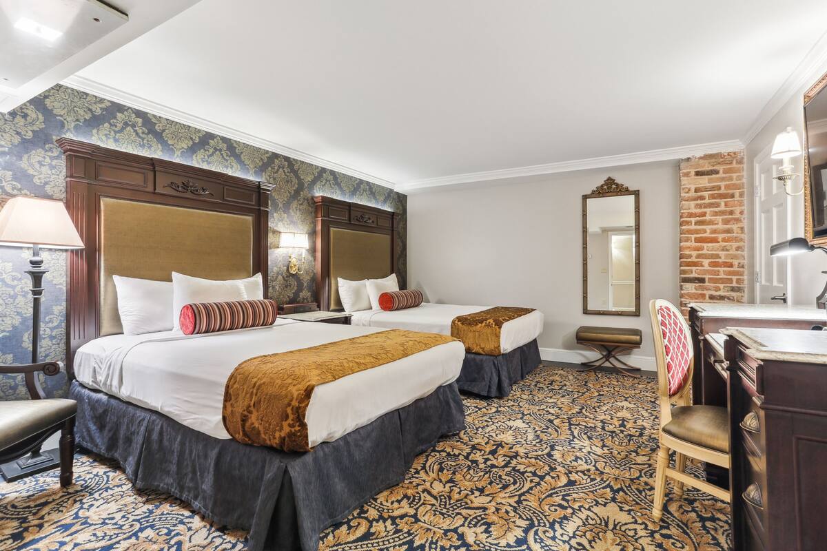 A hotel room with two beds, a desk, a chair, a mirror, and a patterned carpet.