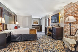 Quarto de hotel com uma cama grande, uma escrivaninha, uma televisão e uma parede de tijolos.