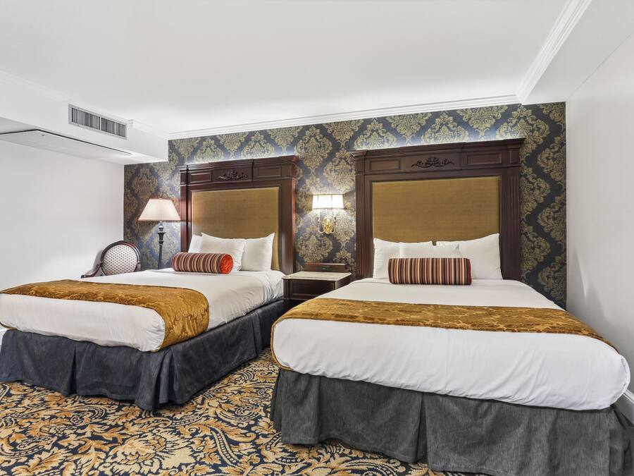 A hotel room with two beds, a patterned carpet, and a decorative wall.