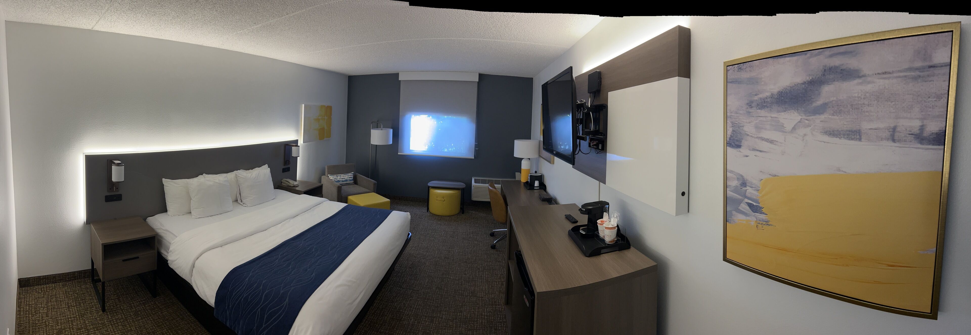 A hotel room with a large bed, a desk with a coffee maker, a TV, and a painting on the wall.