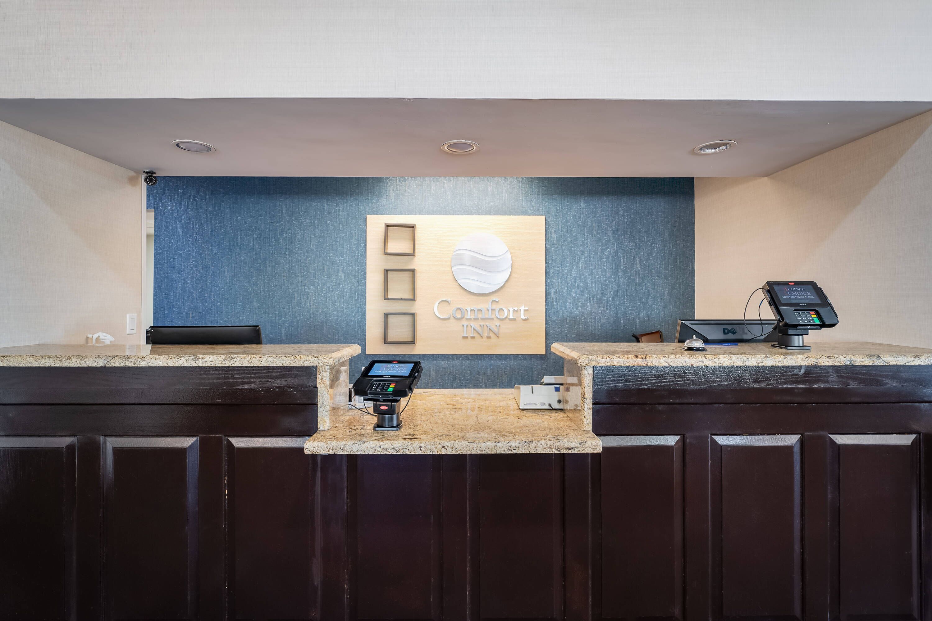 A hotel reception area with a digital kiosk, a cash register, and a sign that reads "Comfort Inn".