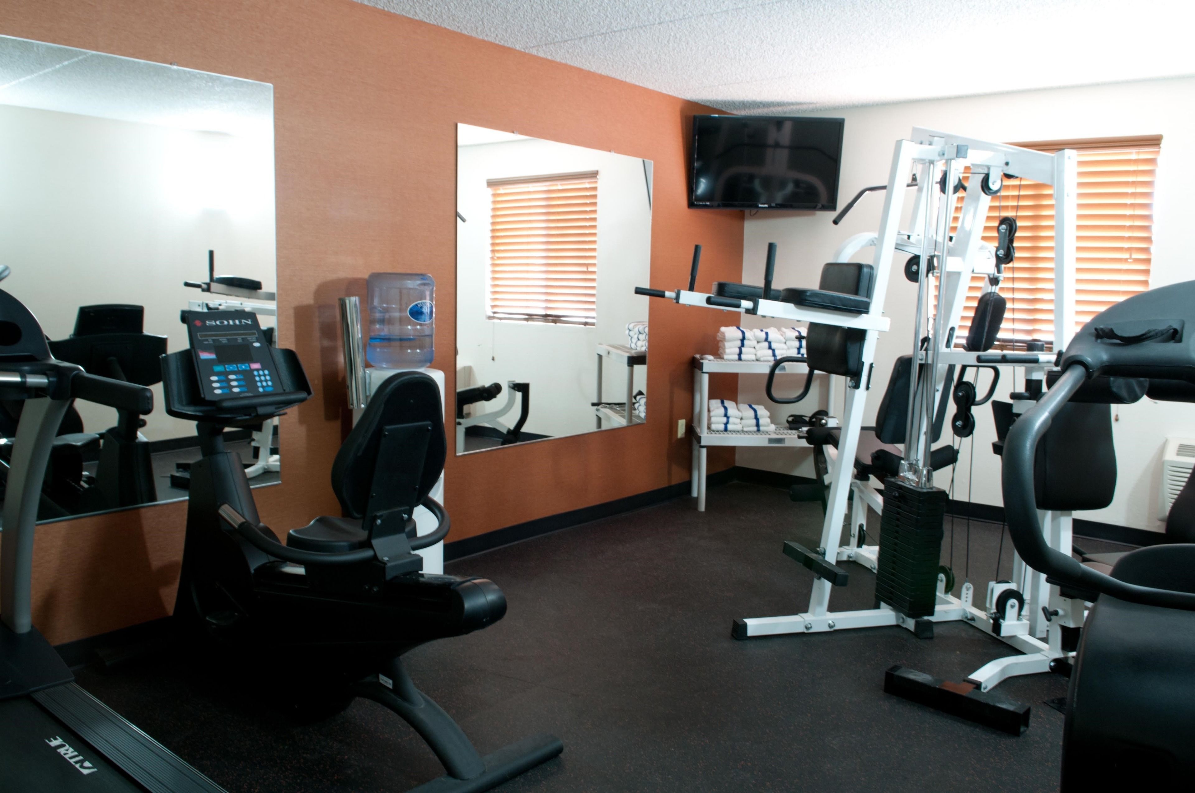 Un gimnasio con equipo de ejercicio, un dispensador de agua y un televisor en la pared.