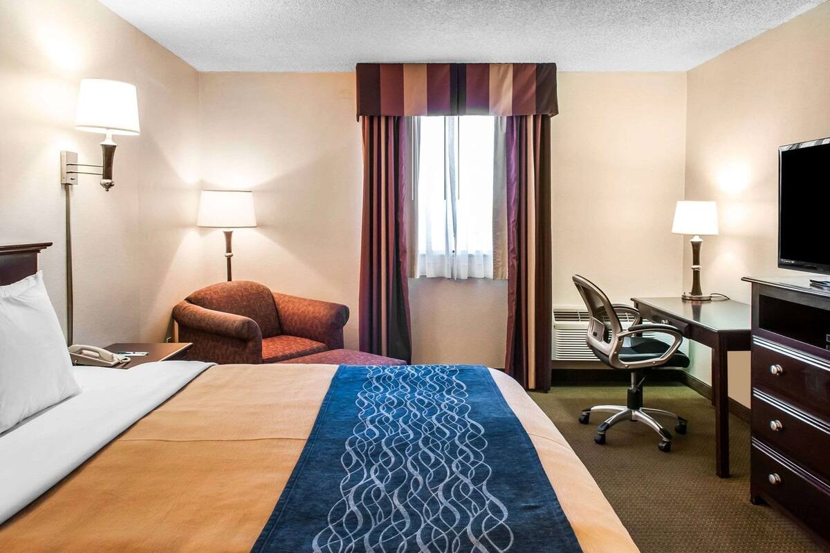 A hotel room with a bed, a desk, a chair, a television, and a window with curtains.
