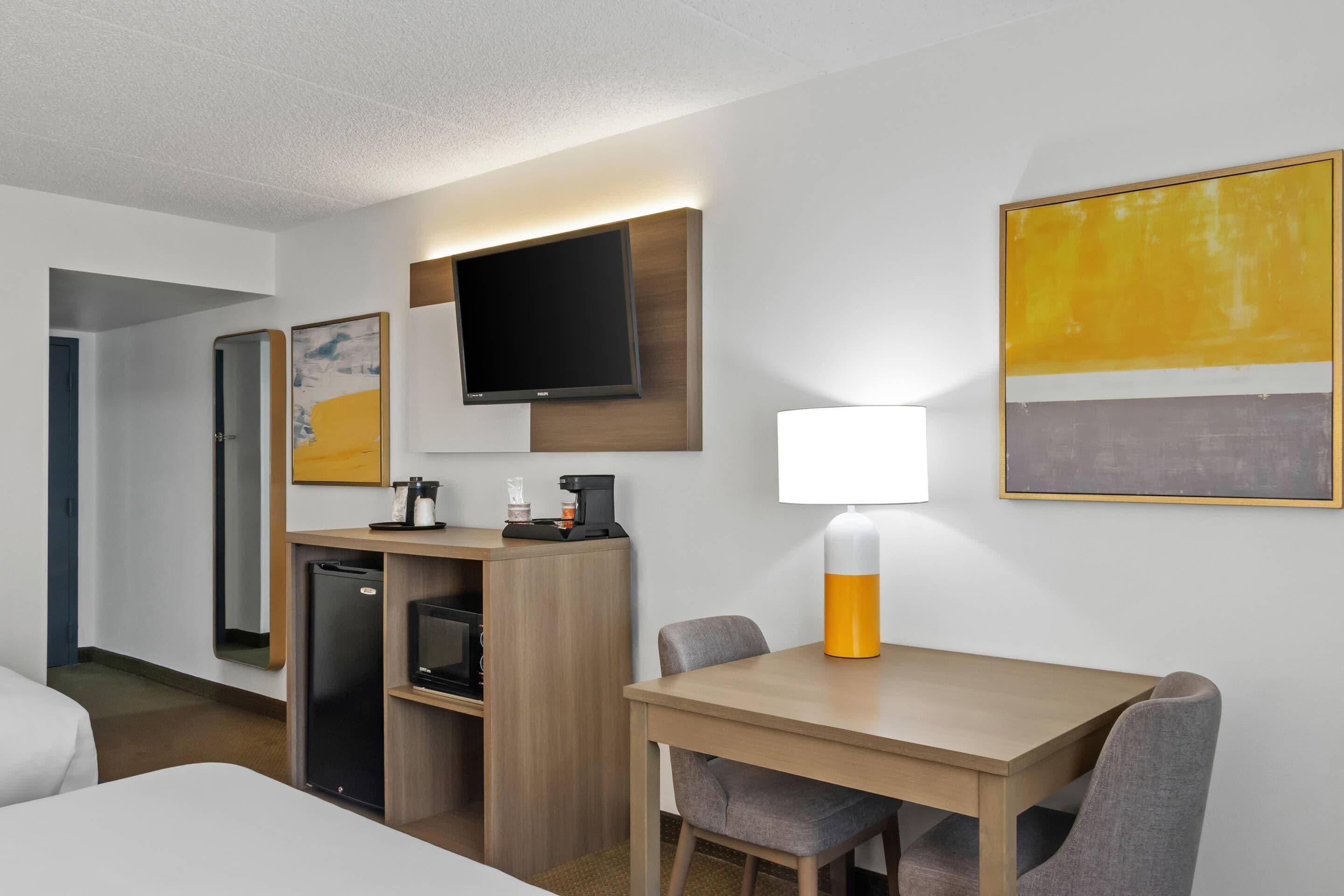 A hotel room with a bed, a desk with a lamp, a television, and artwork on the walls.