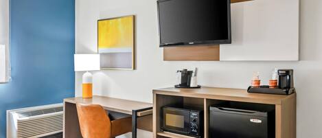 Habitación de hotel con escritorio, silla, televisor de pantalla plana, microondas, refrigerador y cafetera.