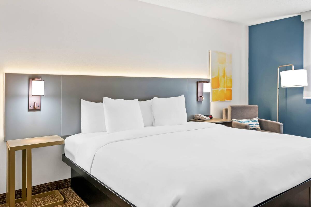 Una habitación de hotel con una cama grande, mesitas de noche, una silla y una lámpara de pared.