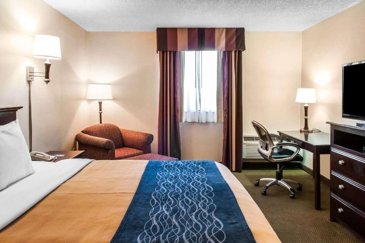 Habitación de hotel con cama, escritorio, silla, televisor y ventana con cortinas.