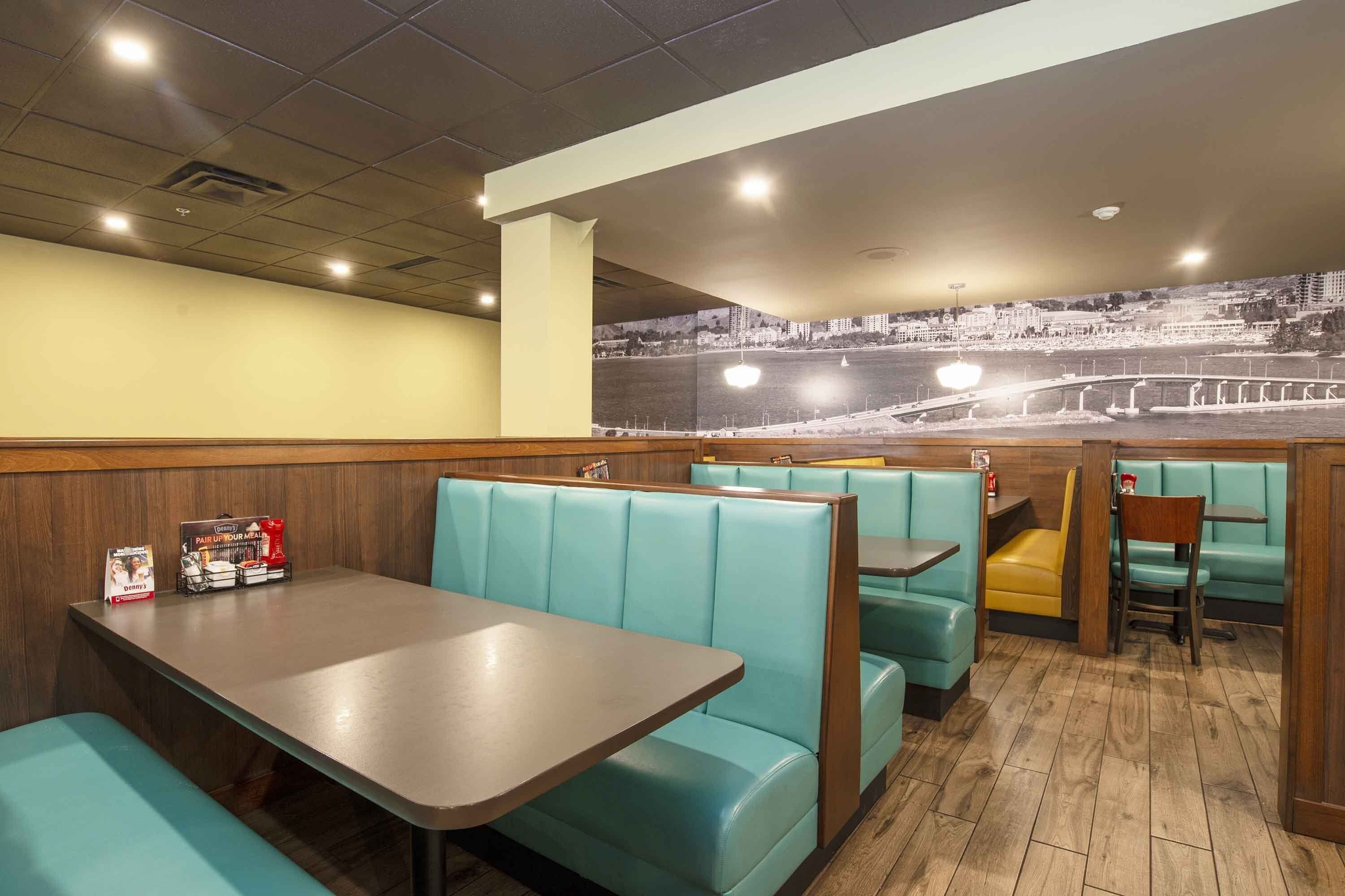 Un interior de restaurante con cabinas color turquesa, mesas de madera y un mural con vista a la ciudad.