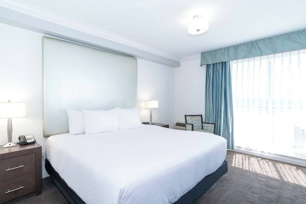 A hotel room with a large bed, a bedside table with a lamp, a phone, and a framed picture.
