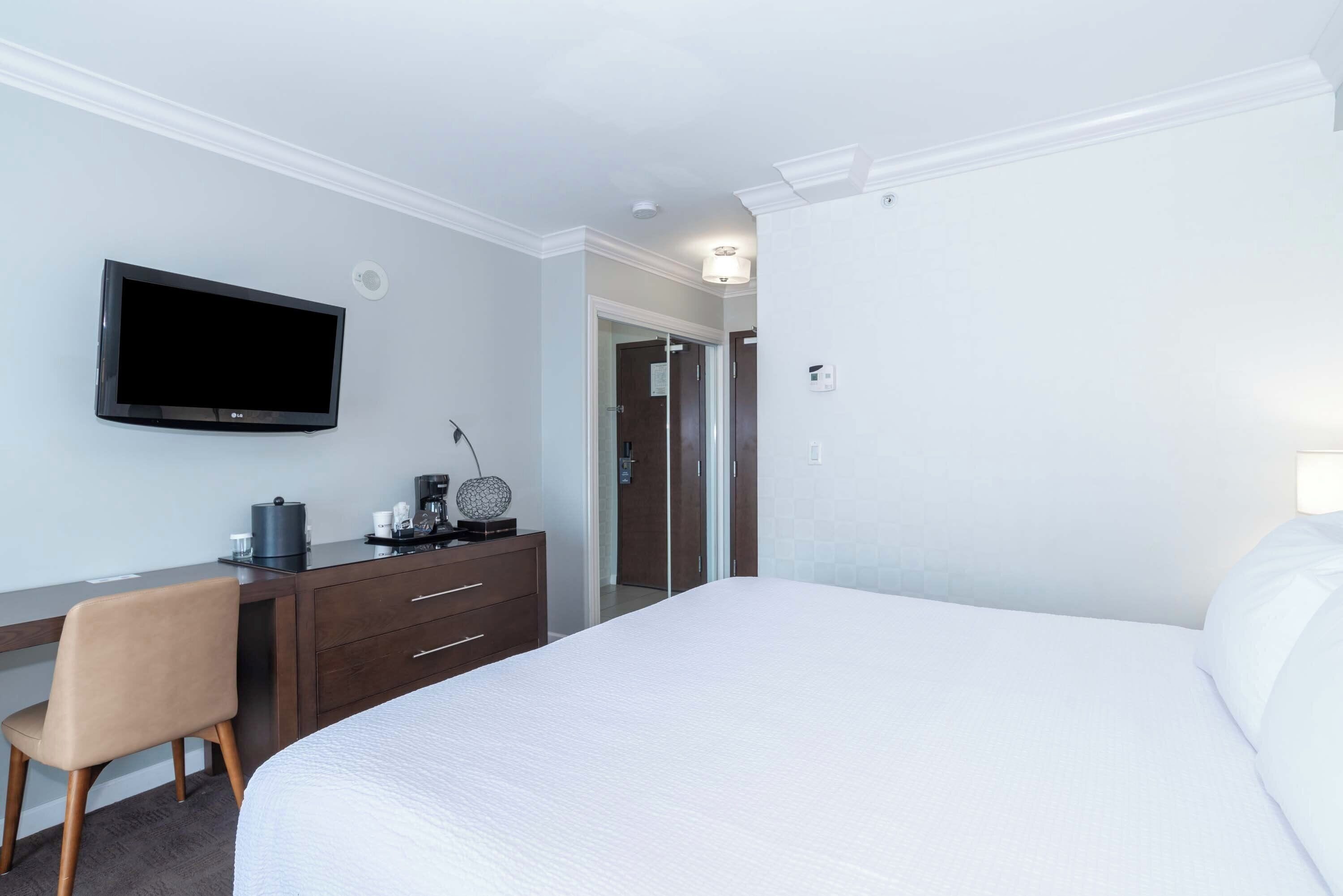A hotel room with a bed, a desk, a chair, a flat-screen TV, and a coffee maker.