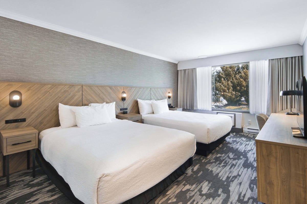 A hotel room with two beds, a desk, a chair, and a large window with curtains.