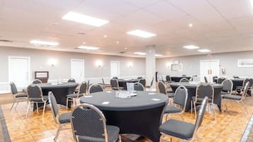 Un salón de conferencias con varias mesas redondas, cada una rodeada de sillas, en un espacio bien iluminado con suelo de baldosas.