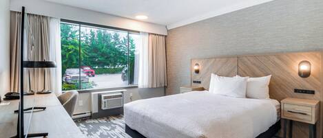 Habitación de hotel con una cama grande, un escritorio con silla, una ventana con cortinas y vistas al exterior.