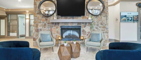 A living room with a stone fireplace, two armchairs, a coffee table, and a flat-screen TV mounted above the fireplace.