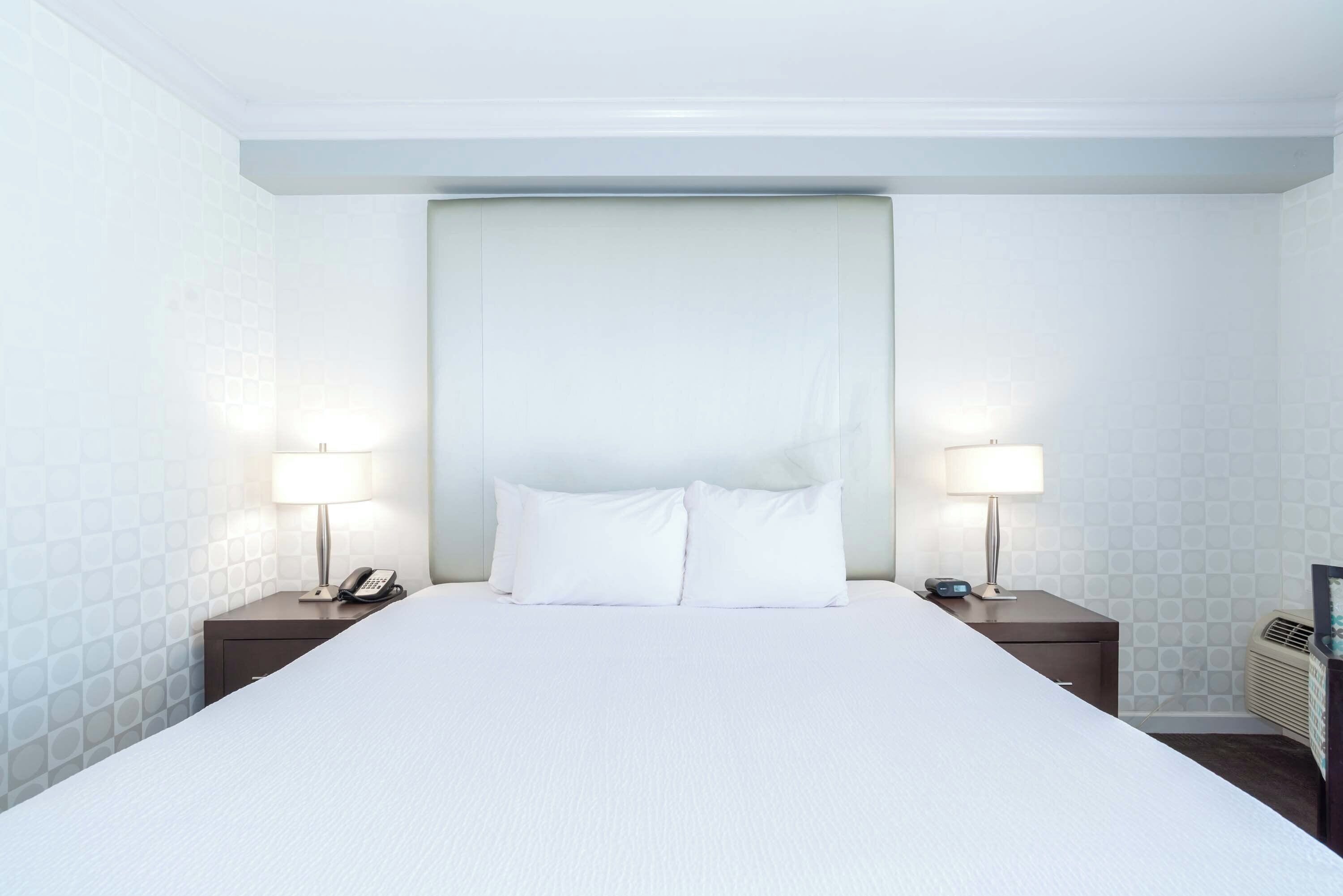 A hotel room with a large bed, two bedside tables with lamps, a telephone, and a wall-mounted air conditioning unit.