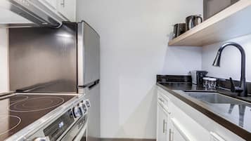 Eine kompakte Küche mit Edelstahl-Kühlschrank, Induktionskochfeld, Mikrowelle und Spüle mit modernem Wasserhahn.