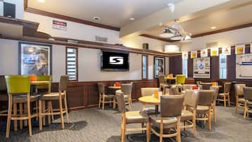 A hotel lobby with wooden chairs, tables, a mounted TV, and a sign indicating a UFC fan cave.