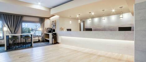 A modern hotel lobby with a reception desk, seating area, and large windows.