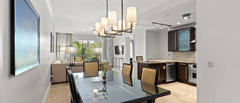 A modern dining area with a glass table, chairs, and a chandelier.