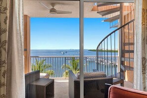 Een balkon met rieten meubilair, uitzicht op zee en een spiltrap.