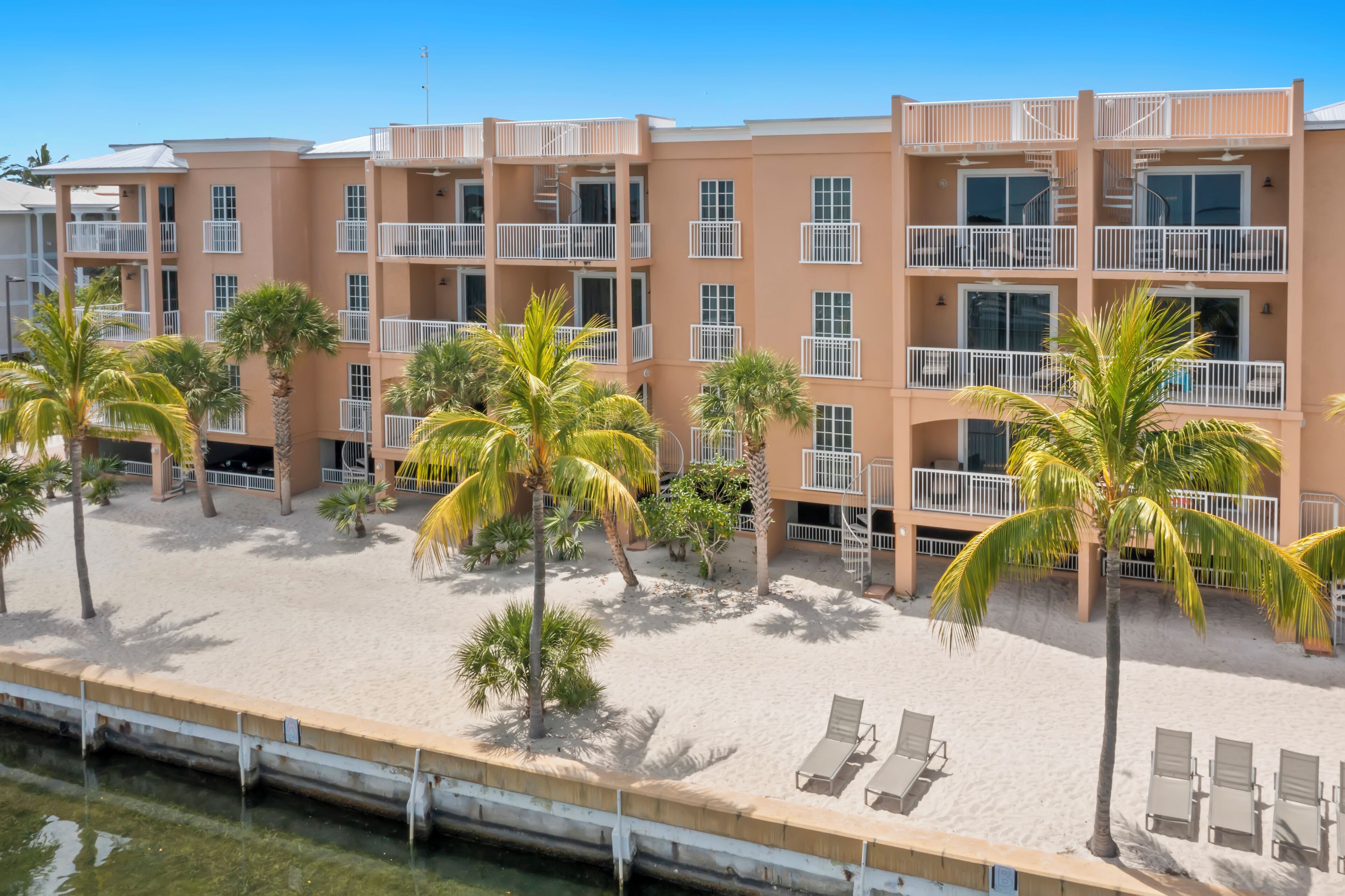 A multi-story hotel with balconies, a sandy beach area, and palm trees.