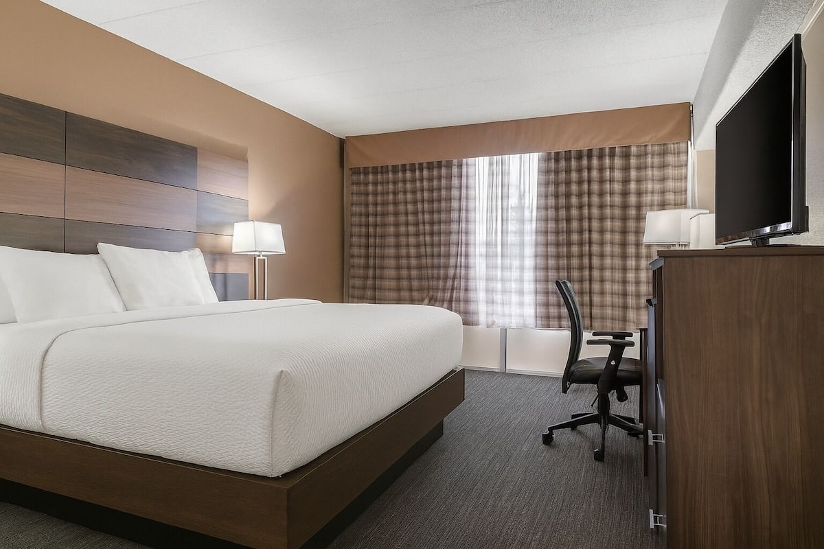 Una habitación de hotel con una cama grande, un escritorio con silla, un televisor y una ventana con cortinas.
