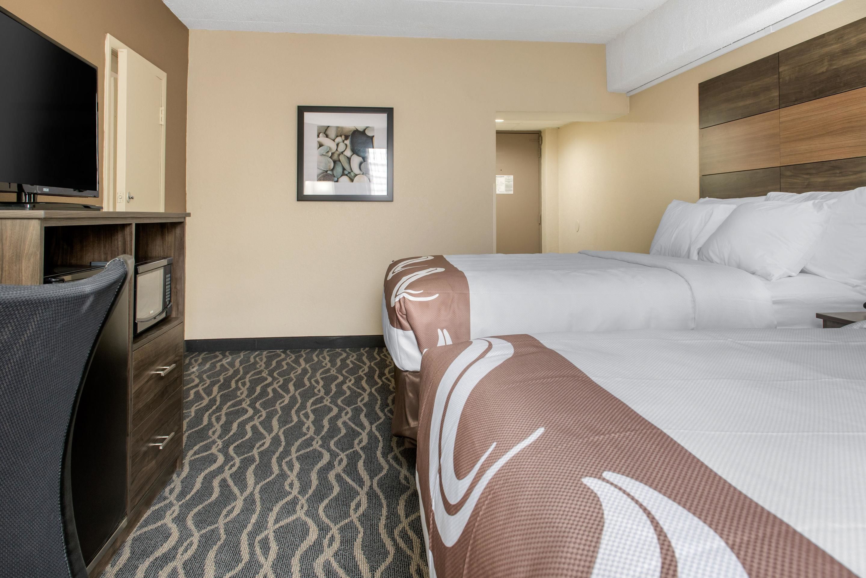 A hotel room with a bed, a TV, a desk, and a patterned carpet.