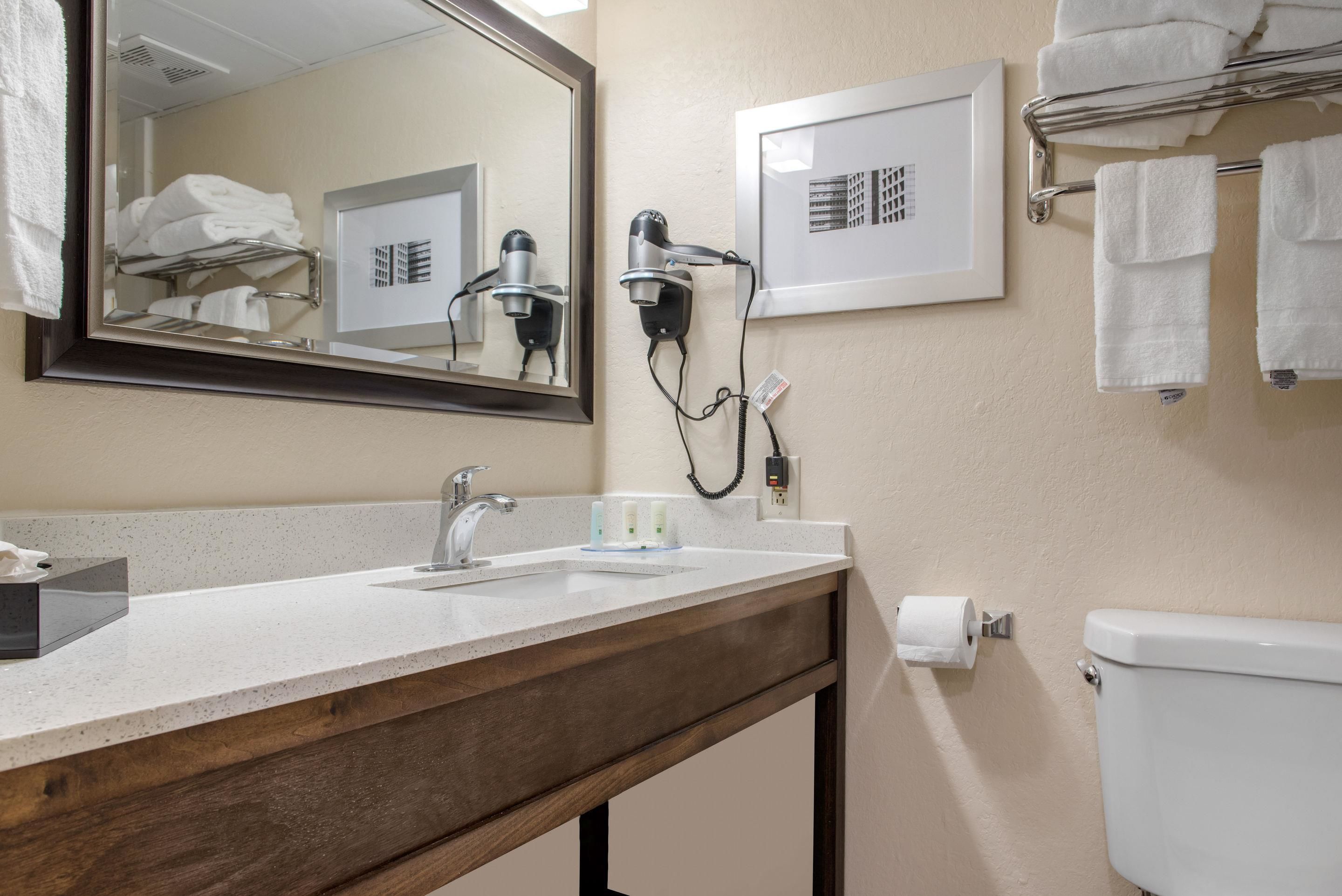 Ein Badezimmer mit Waschbecken, Spiegel, Fön, Handtuchhalter und Toilette.