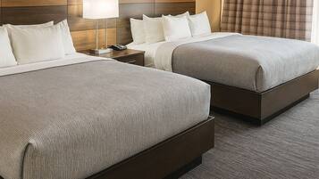 A hotel room with two beds, a nightstand, a lamp, and a window with curtains.