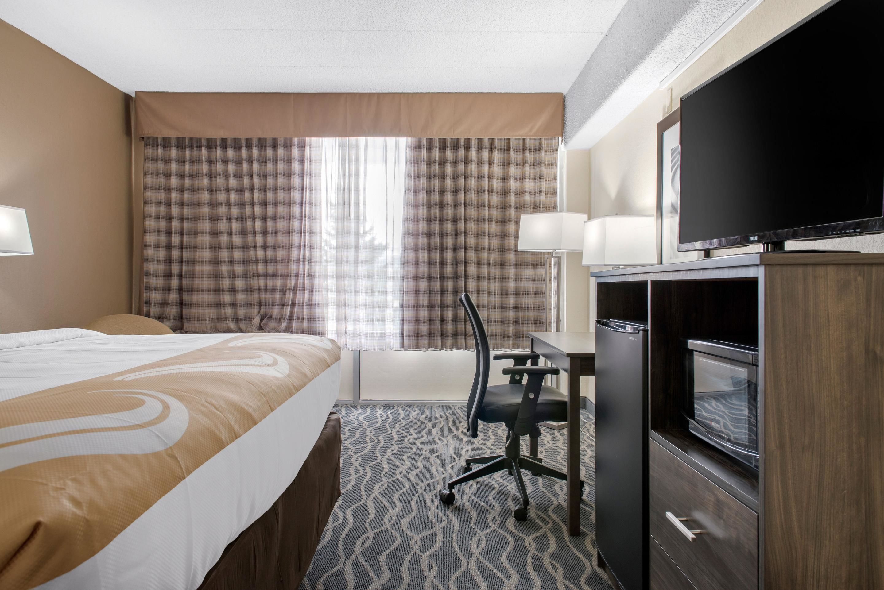 A hotel room with a bed, desk, chair, television, and a minibar.
