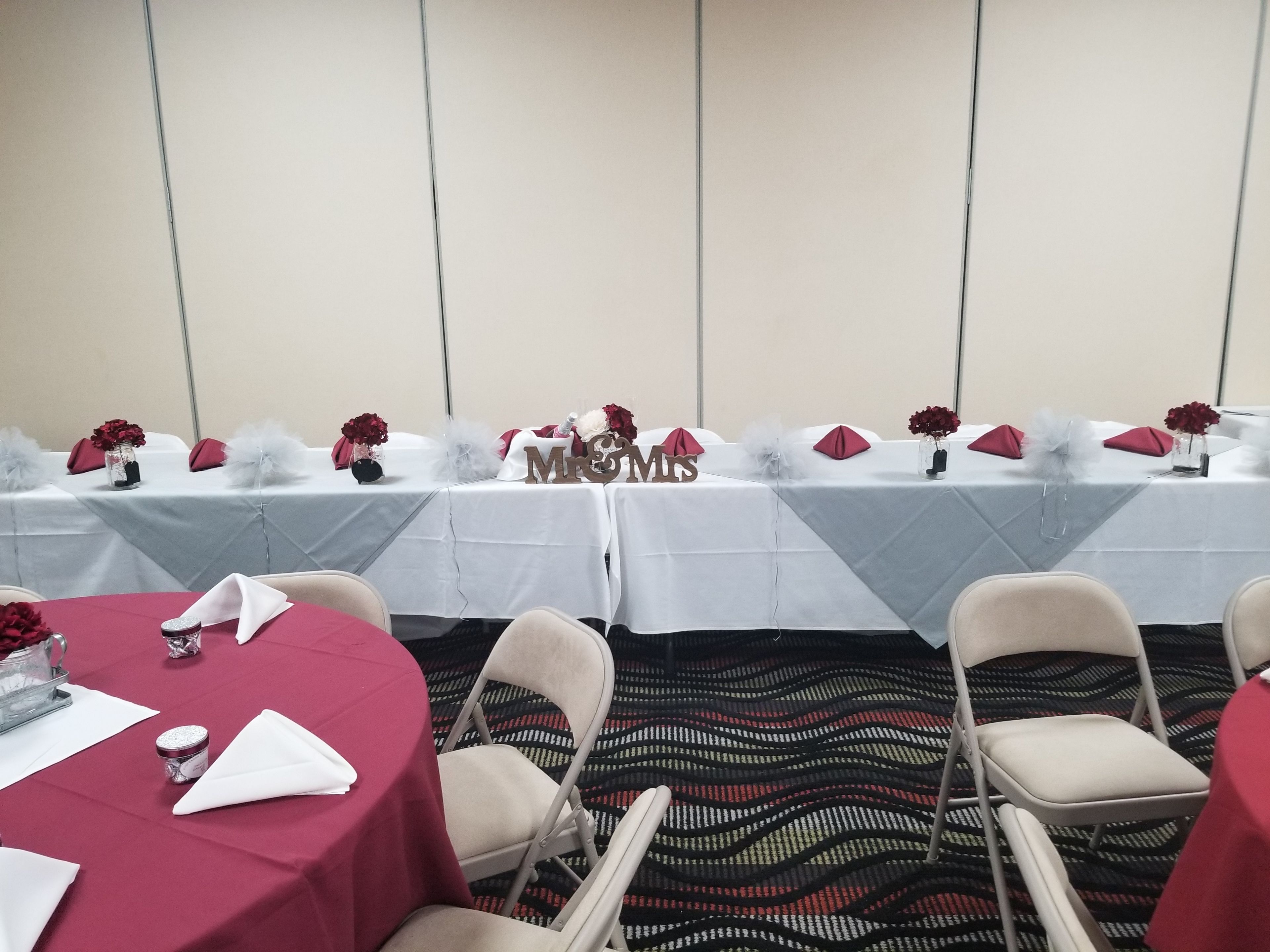 Une salle de conférence avec des tables préparées pour une réunion, agrémentées de nappes blanches, de serviettes rouges et de centres de table floraux.