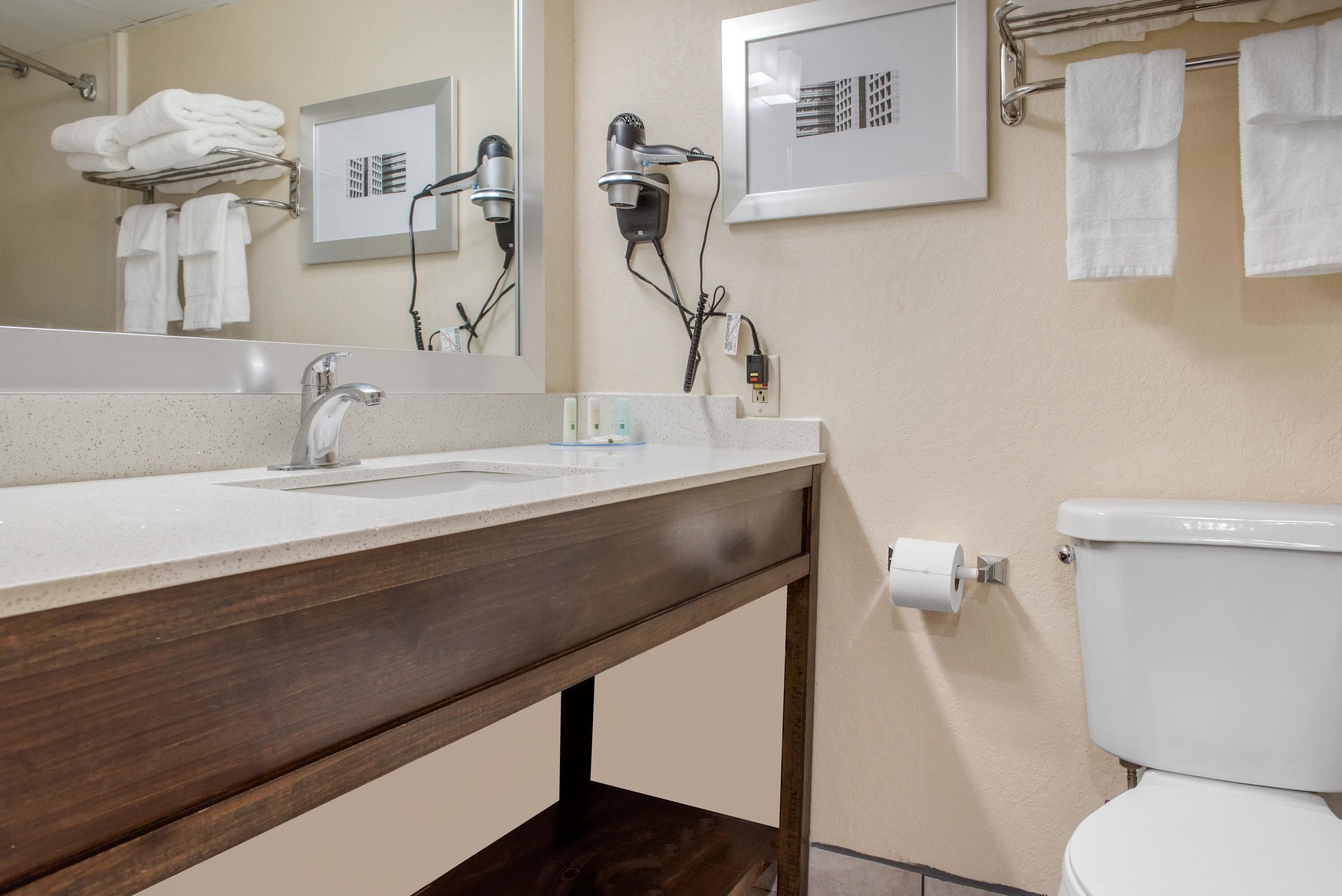 A bathroom with a wooden vanity, a large mirror, a hairdryer, and a toilet.