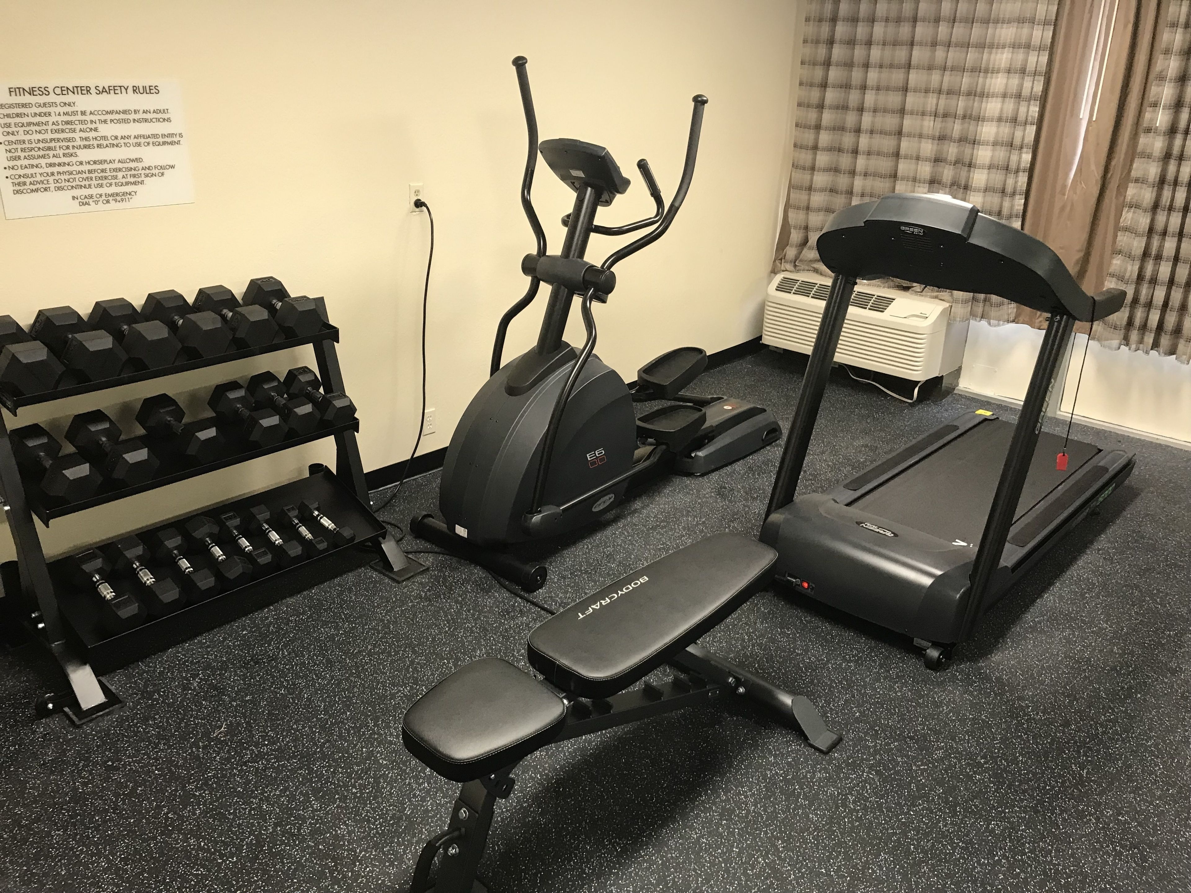 A fitness center with a treadmill, elliptical, and dumbbells.