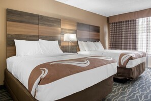 A hotel room with a large bed, a smaller bed, a nightstand, a lamp, and a window with curtains.